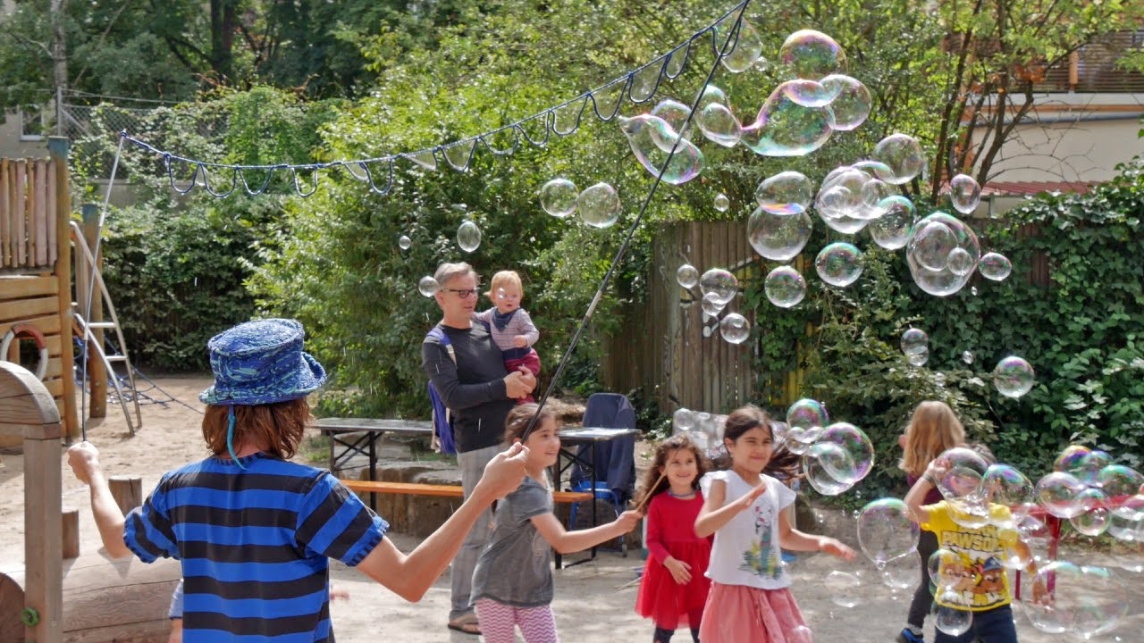 Eine Familie mit Kindern jagt auf dem Spielplatz fr&ouml;hlich einer Wolke aus Seifenblasen nach
