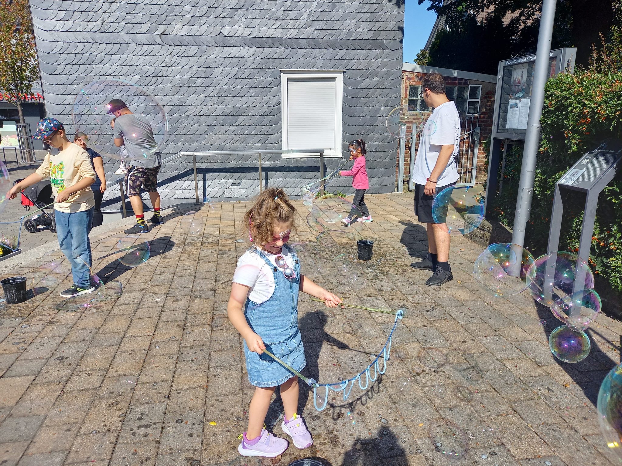 Kinder und Erwachsene machen bei einer Mitmachstation im Sonnenschein gemeinsam Seifenblasen