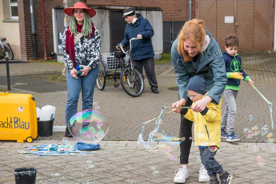 Eine Mutter hilft ihrem Kind beim Stra&szlig;enfest, mit Rogers Material eine Riesenseifenblase zu formen